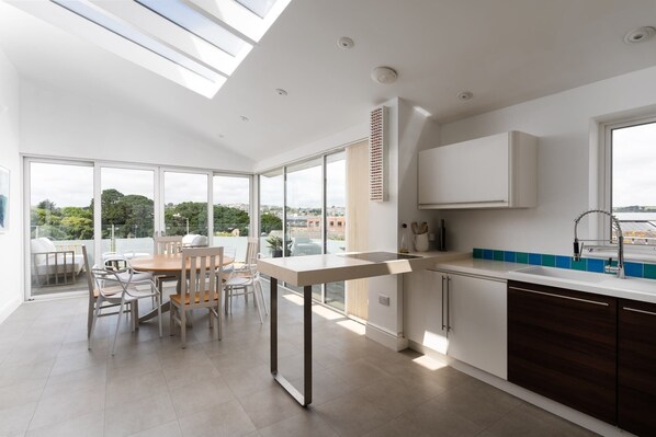 A modern kitchen with a dining area, large windows, and a view of the city. - Spacious House nr Castle Beach, Parking & Sauna (Cornwall)