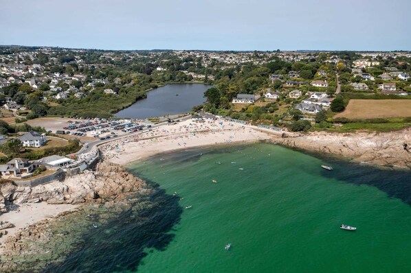 An aerial view of a coastal town with a beach, a parking area, and residential buildings.