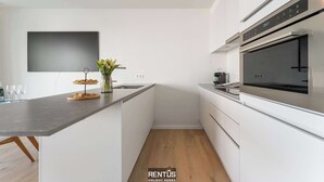 Una cocina moderna con armarios blancos, horno empotrado y una isla grande con encimera oscura.