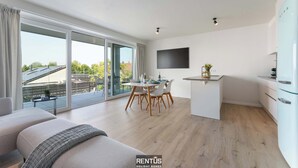 Un apartamento moderno con comedor, sofá, televisor y cocina.