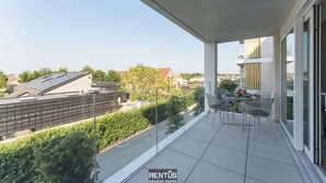 Un balcón con una mesa y sillas, con vista a una zona residencial que incluye casas y una calle.
