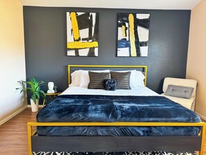 A modern bedroom with a bed, a chair, and two abstract paintings on the wall. - Spacious 4BR Family Retreat: King bed, WI-FI & Parking (Las Vegas)