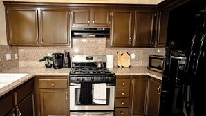 Una cocina con gabinetes marrón oscuro, una estufa de acero inoxidable, un microondas y un refrigerador negro.