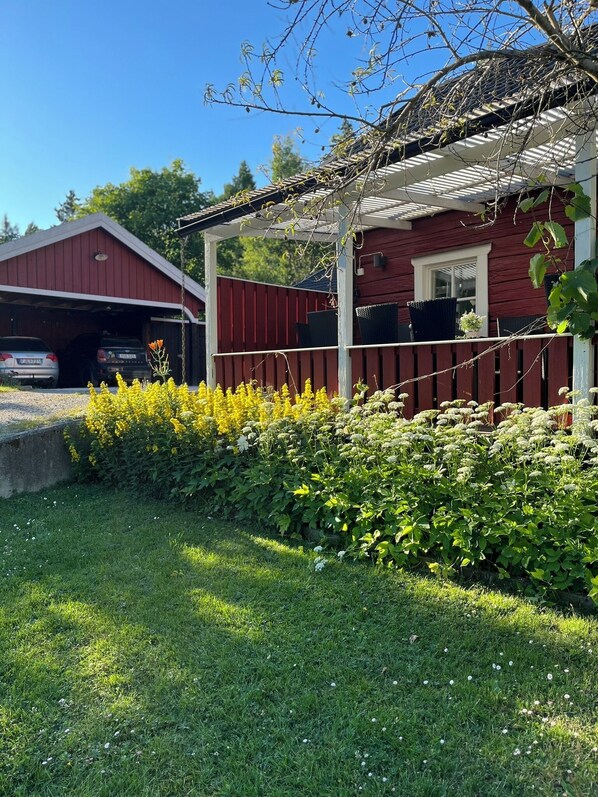 Un bâtiment rouge doté d’un porche abrité, d’un garage et d’un jardin bien entretenu, agrémenté de fleurs jaunes et d’arbustes verts.