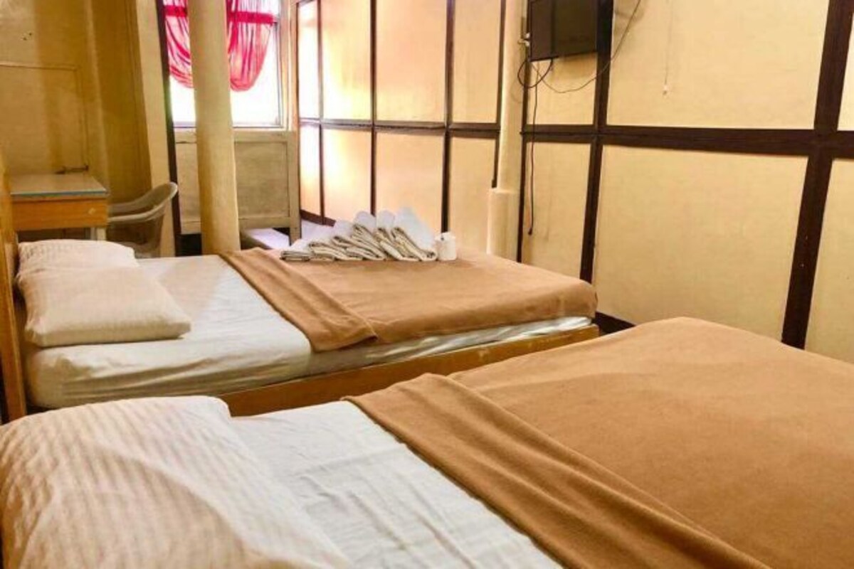 Una habitación con dos camas, una mesita, una silla y una ventana con cortinas.