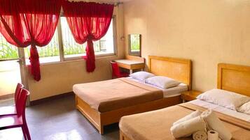 A room with two beds, a desk, a chair, and a window with red curtains.