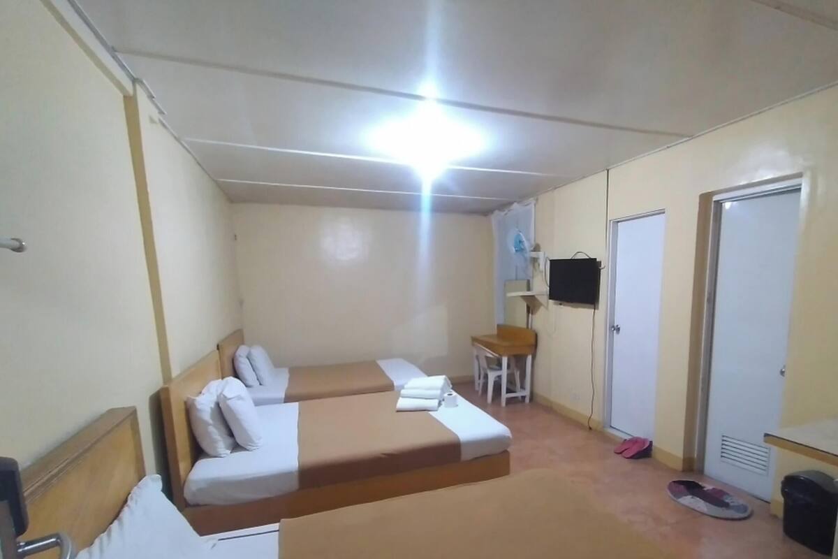 Una habitación con dos camas, un escritorio, una silla, un televisor y una puerta.