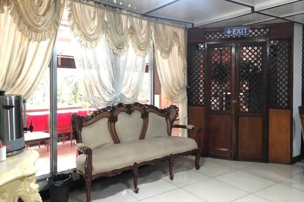 Una habitación con sofá, cortinas, señal de salida y ventana con vista a un espacio exterior.