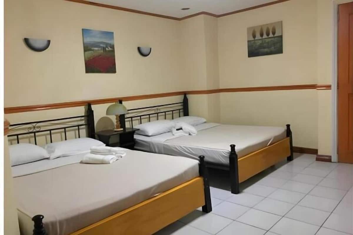 Una habitación de hotel con dos camas individuales, una mesita de noche con lámpara y un cuadro en la pared.