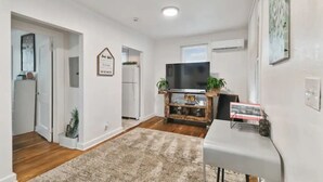 A modern living room with a flat-screen TV on a wooden stand, a white console table, and a beige rug. - 1920s Cottage Downtown, Ybor with Hot Tub! (Tampa)
