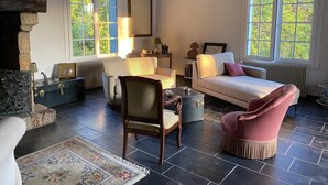 A room with a fireplace, a sofa, a chair, a table, and a large window with a view of greenery.