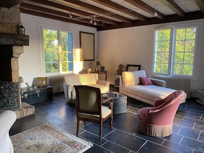 A room with a fireplace, a sofa, a chair, a table, and a large window with a view of greenery.