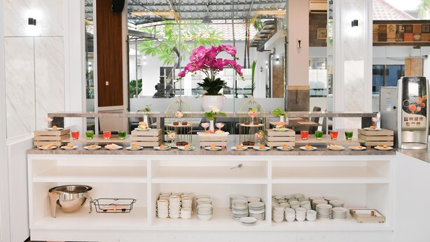 Un buffet proposant une variété de plats et agrémenté d’un grand arrangement floral central composé d’orchidées roses.