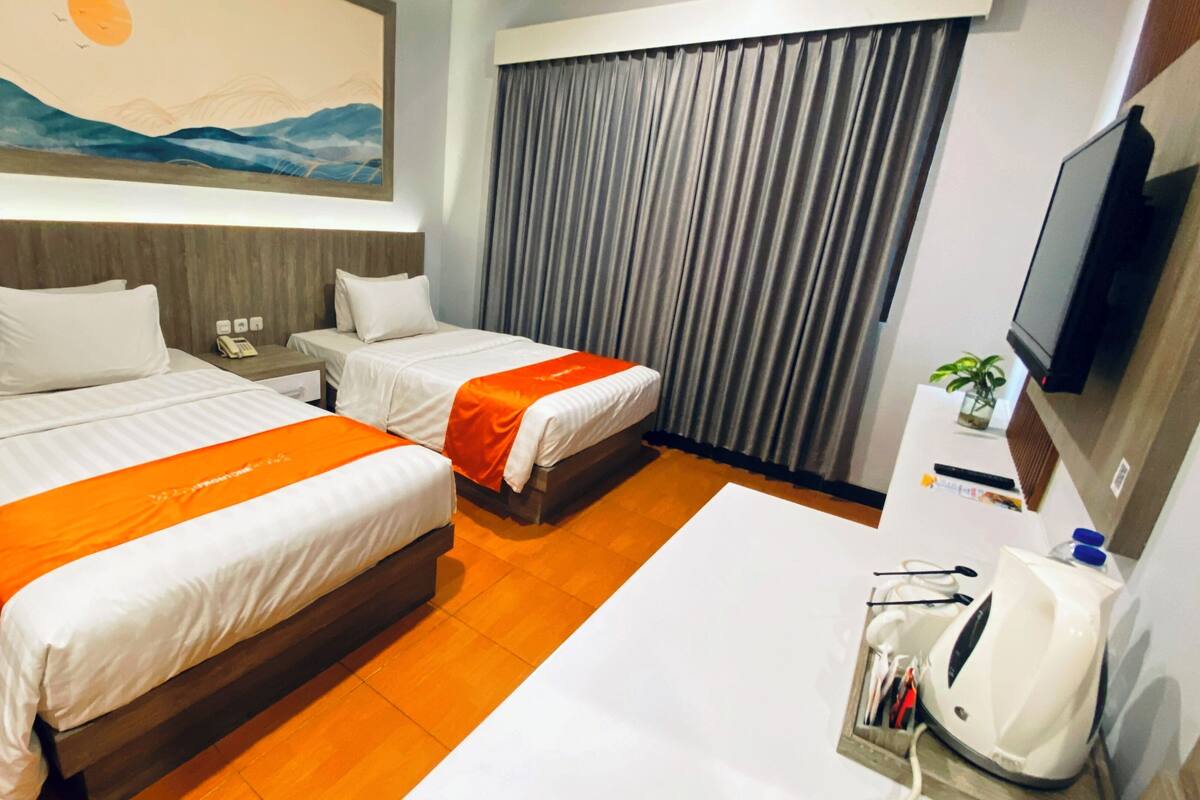 A hotel room with two beds, a desk, a TV, and a painting on the wall.
