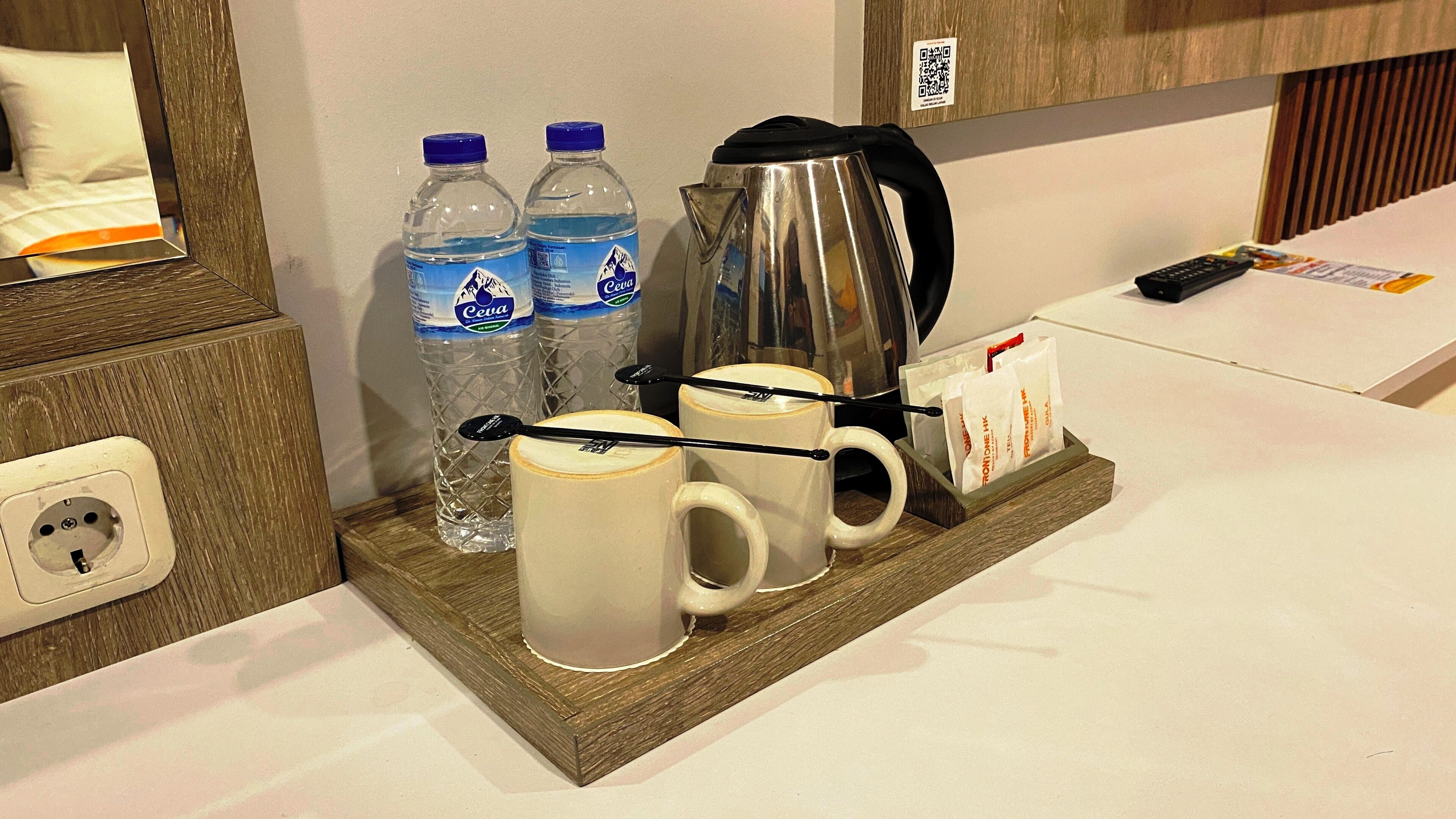A hotel room's breakfast area with a wooden tray holding two water bottles, a coffee pot, two mugs, and a box of tea bags.