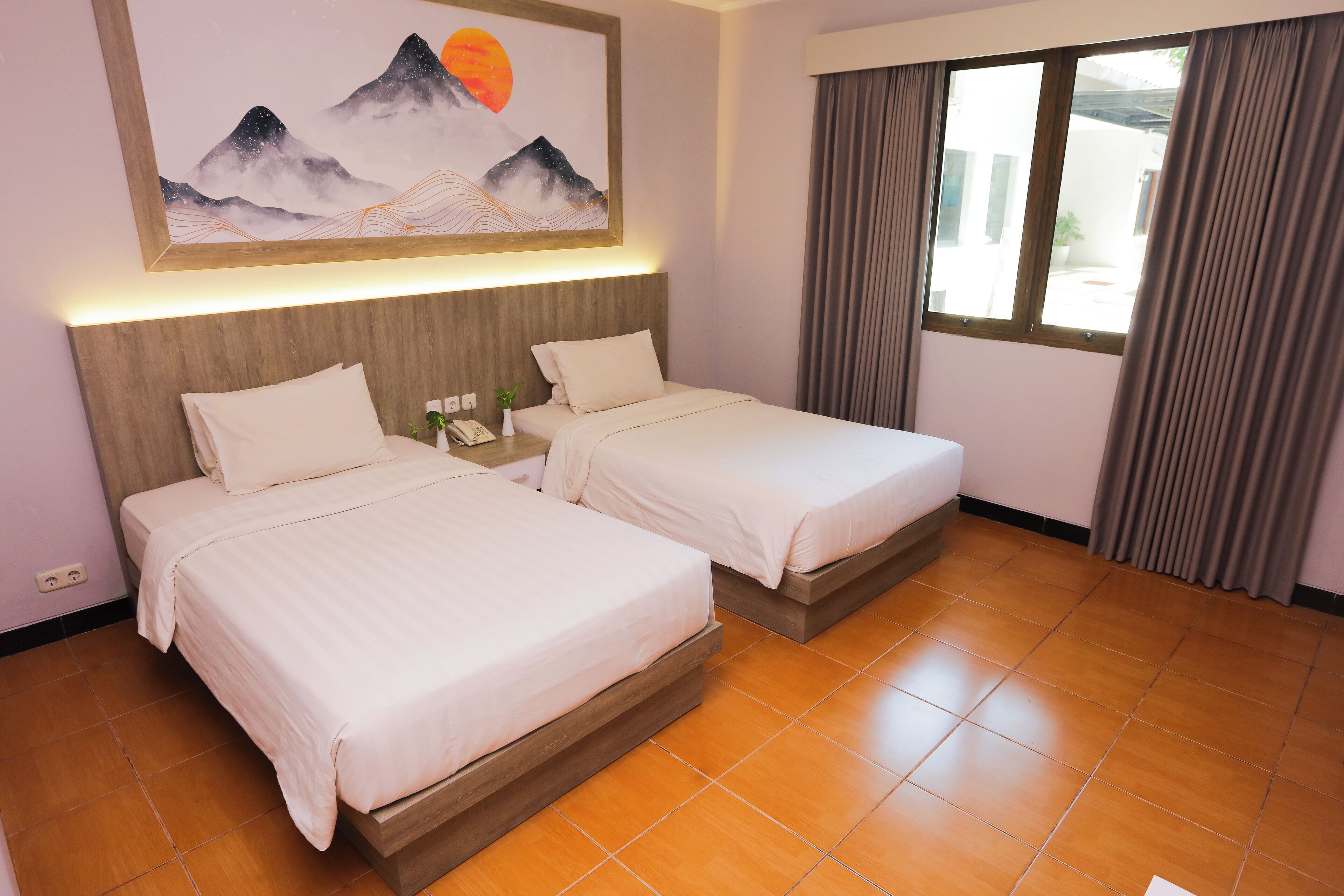 A hotel room with two beds, a painting of mountains, a window with curtains, and a tiled floor.