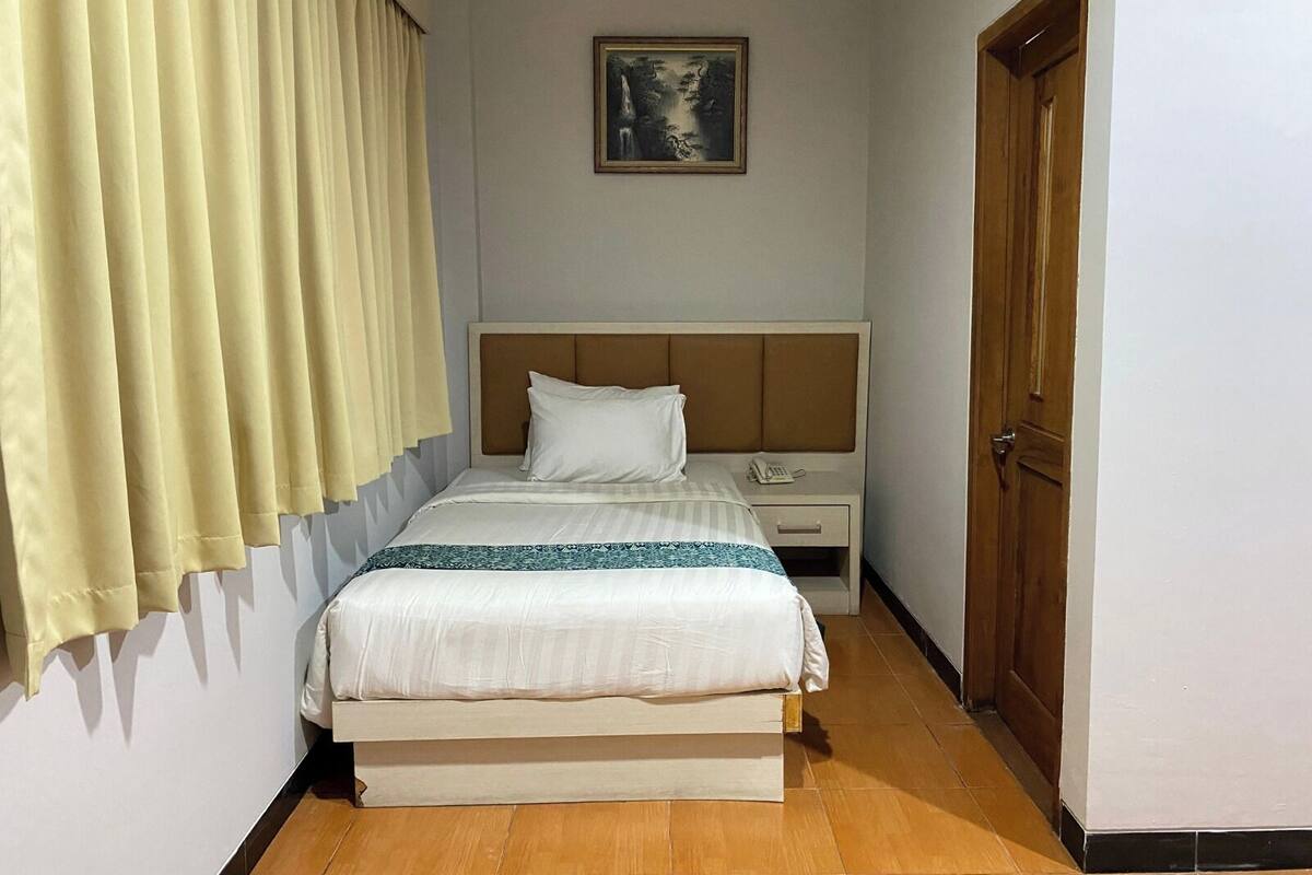 A hotel room with a bed, a nightstand, a telephone, a painting on the wall, and a door.