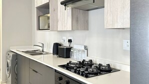 A modern kitchen with grey cabinets, a stainless steel refrigerator, a built-in oven, and a gas stove. - The Oasis 92 on New Midrand (Midrand)