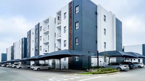 A multi-story residential building with a modern design, featuring balconies and a parking area with cars. - The Oasis 92 on New Midrand (Midrand)