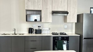 A modern kitchen with grey cabinets, a stainless steel refrigerator, and a built-in oven. - The Oasis 92 on New Midrand (Midrand)