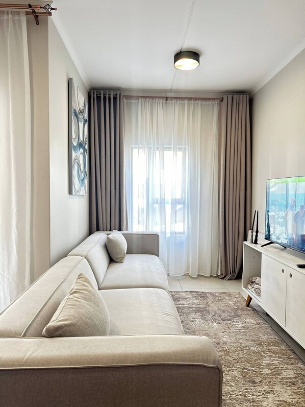 Un salon moderne avec un canapé, un téléviseur à écran plat et une grande fenêtre avec des rideaux.