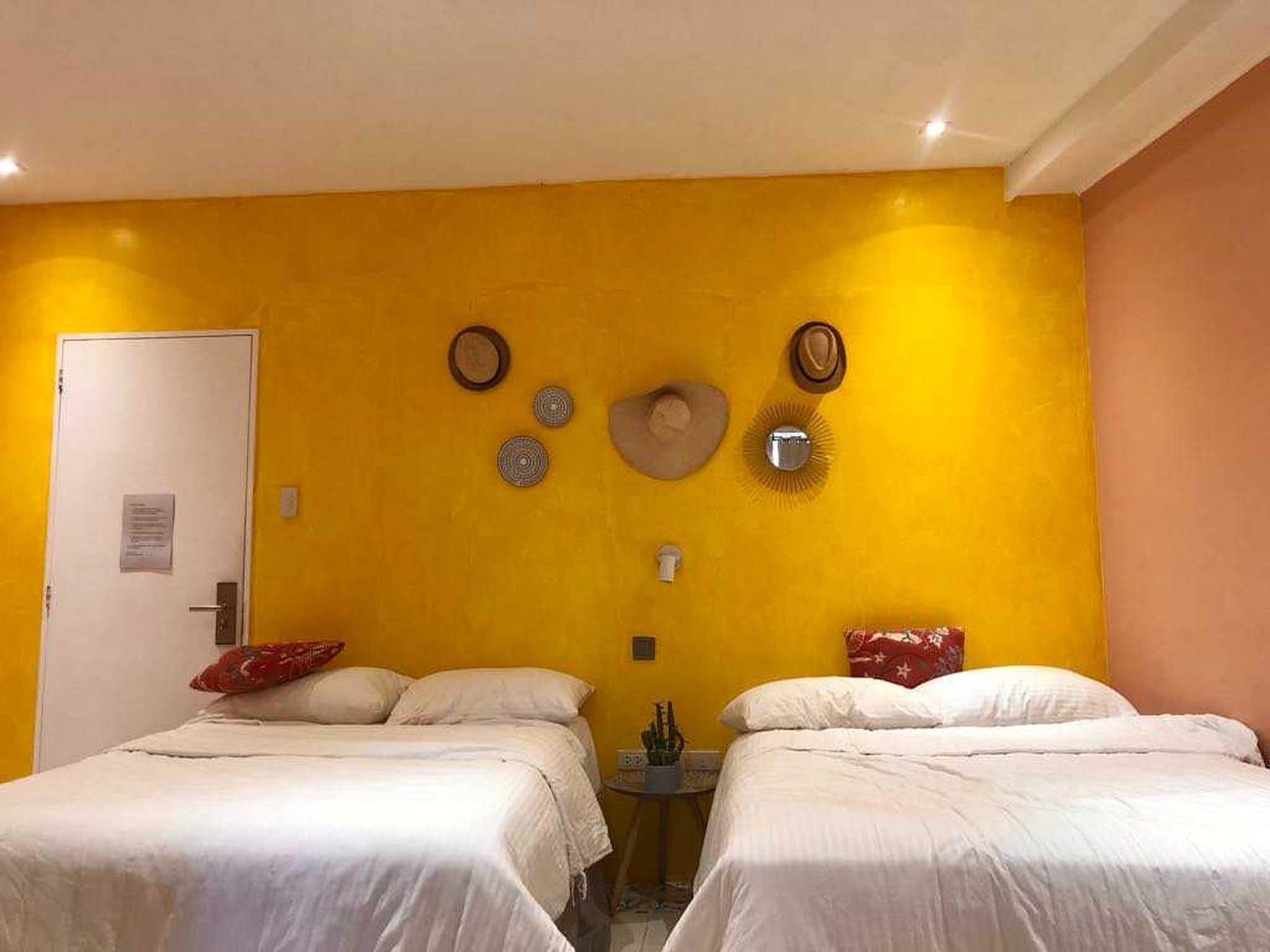A room with two beds, a door, and wall decorations including a hat and circular items.