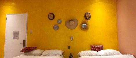 Una habitación con dos camas, una puerta y adornos en la pared, incluyendo un sombrero y objetos circulares.