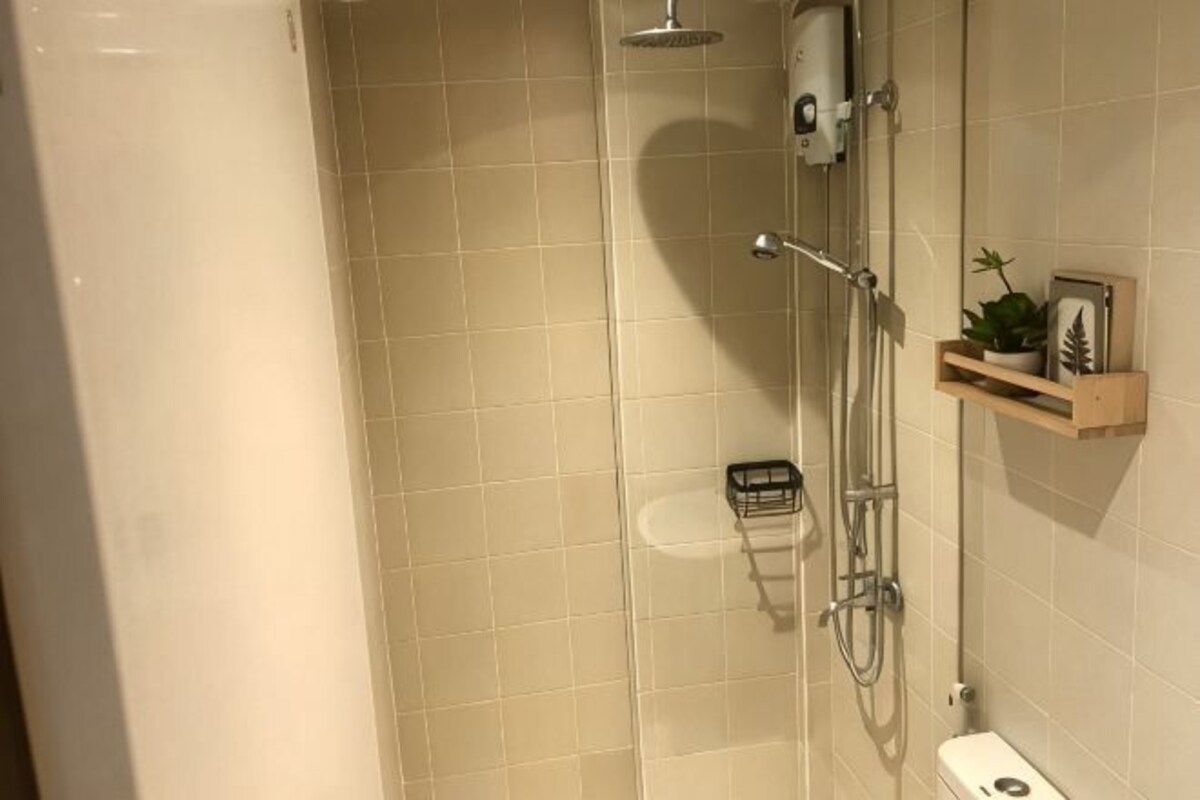 A bathroom with a shower, toilet, and a shelf with a plant and a picture.