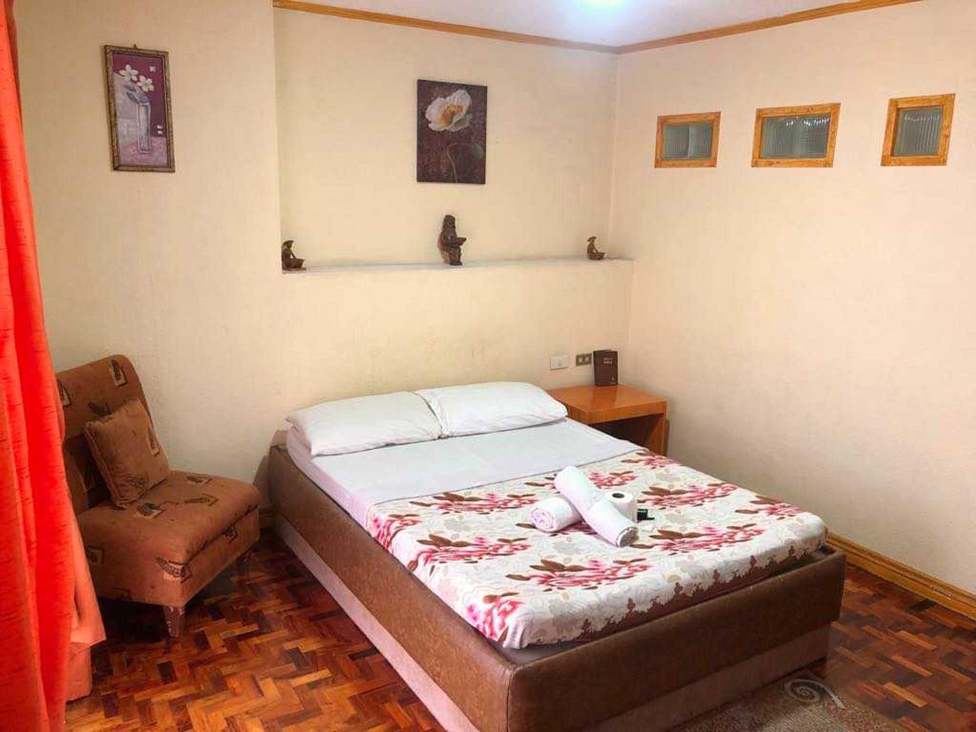 A bedroom with a bed, a chair, a shelf with decorative items, and a window with blinds.