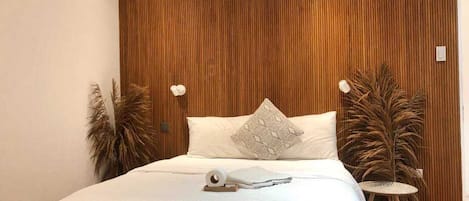 Un dormitorio con cabecera de madera, ropa de cama blanca y dos mesitas de noche con lámparas.