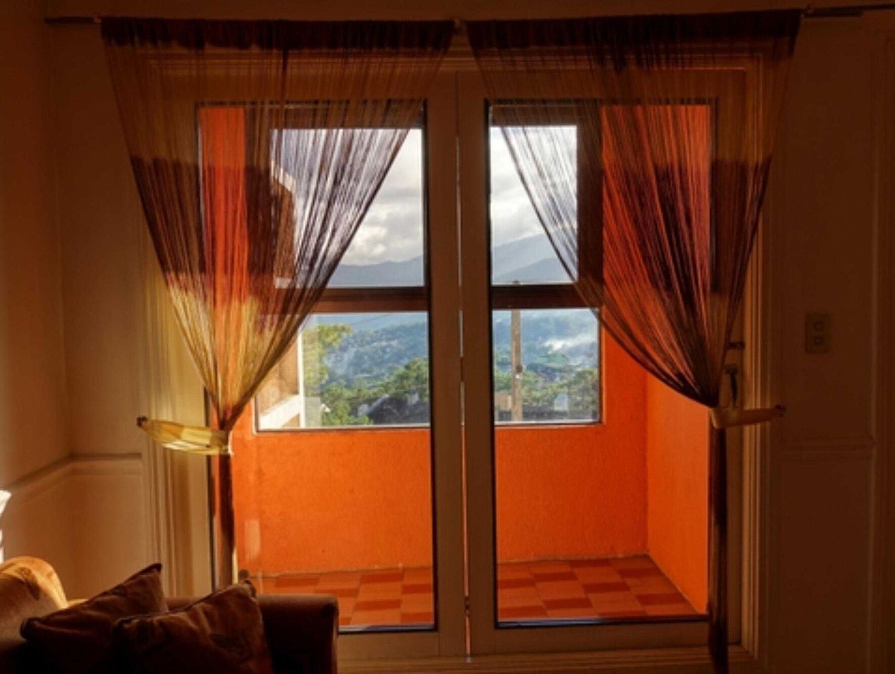 Una habitación con ventana, cortinas, una silla y vistas al paisaje.