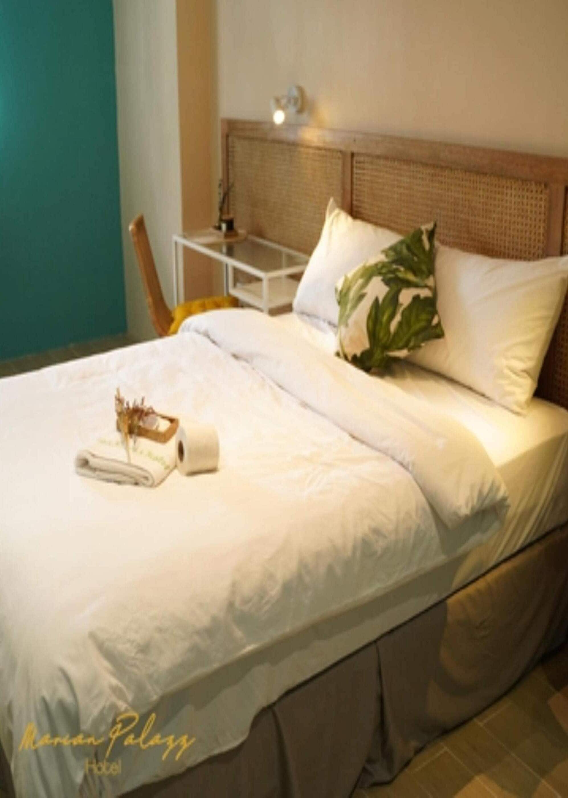 Un lit bien fait, avec du linge de lit blanc, une table de chevet avec une lampe et une plante en pot posée sur la tête de lit.