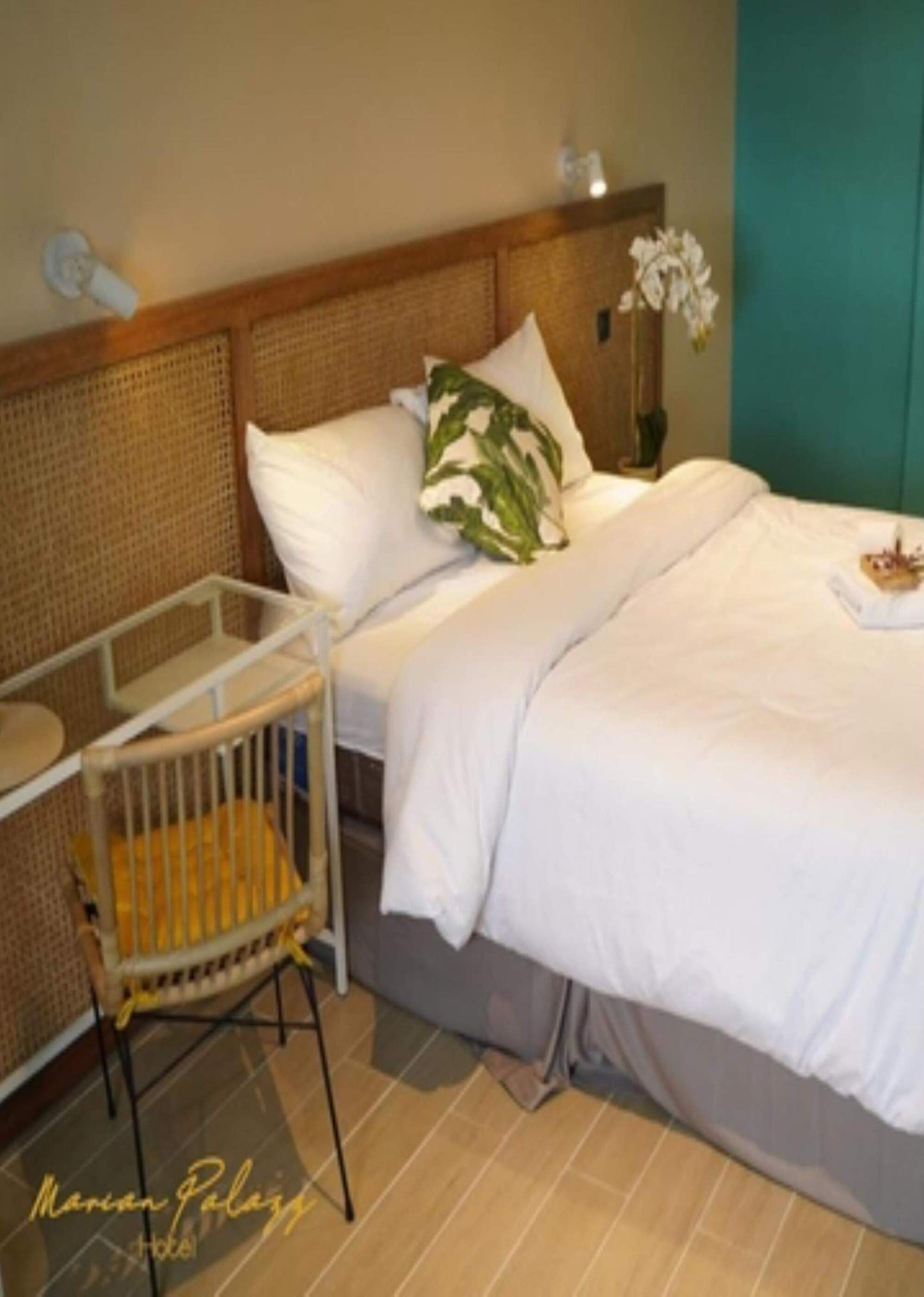 A hotel room with a bed, a crib, a vase with flowers, and a teal wall.