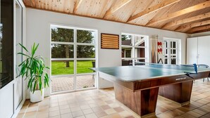 Une table de billard dans une pièce dotée d’un plafond en bois, de grandes fenêtres et d’une plante en pot.