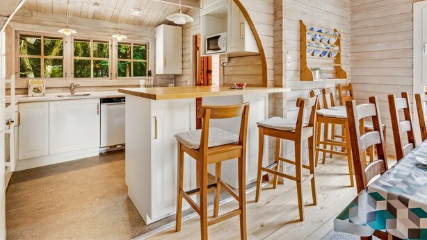 L’intérieur d’un chalet en bois comprend une cuisine, un coin repas et une grande fenêtre donnant sur un paysage verdoyant.
