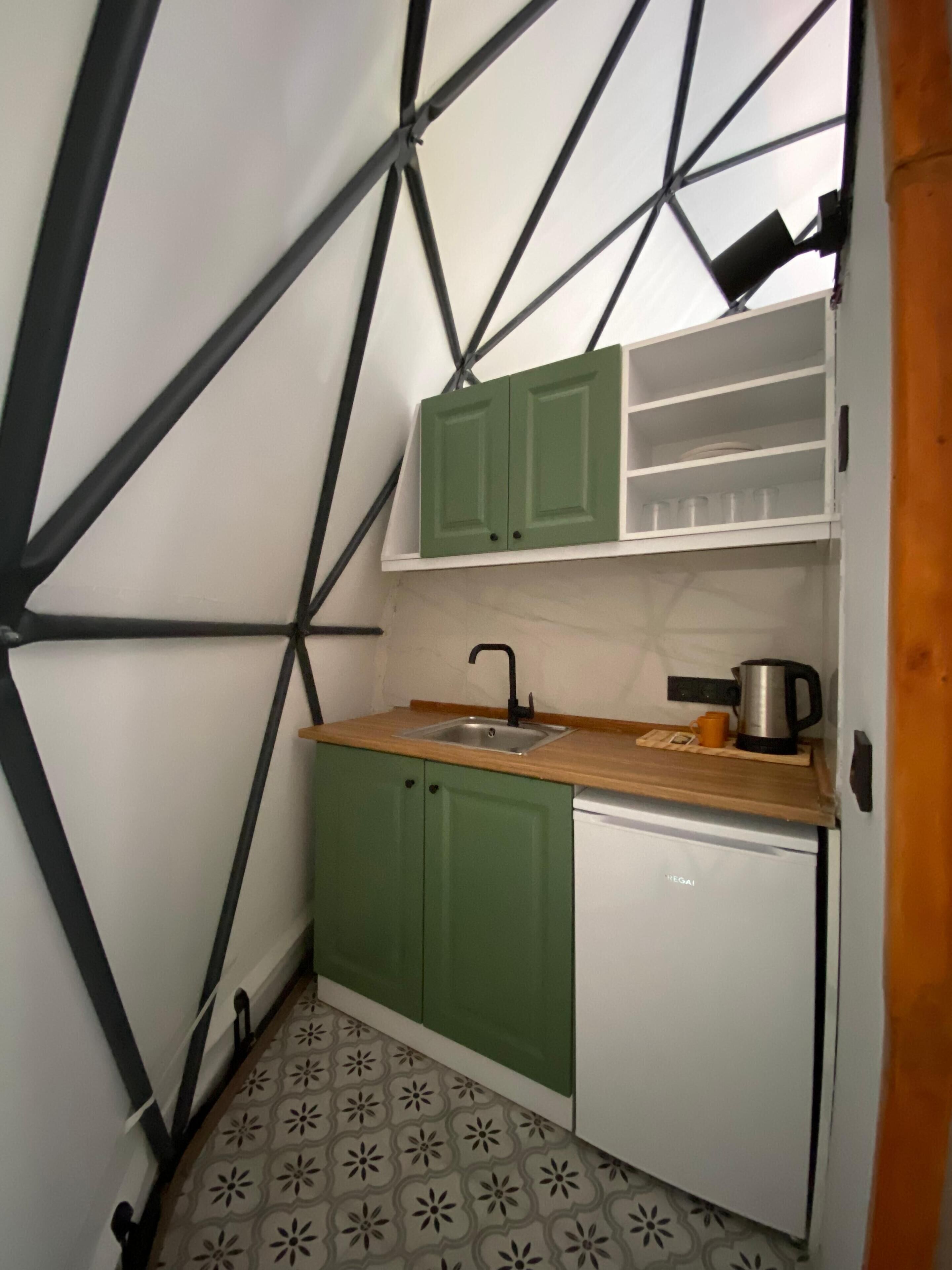 A compact kitchen with green cabinets, a white dishwasher, and a wooden countertop.
