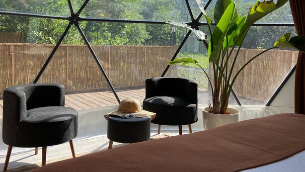 A room with a large window, a bed, two black chairs, a small round table, and a potted plant. - EVALAND GLAMPING RESORT (Ardesen)