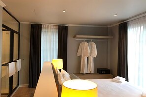 Une chambre d’hôtel comprenant un lit, une table de chevet avec une lampe, un miroir, une armoire et une fenêtre avec des rideaux.