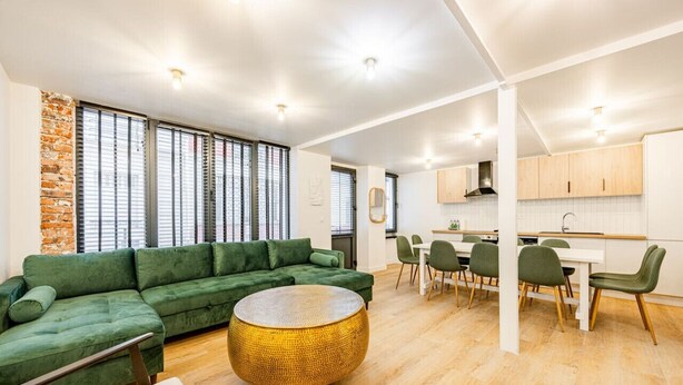 A modern living room with a green sofa, a round woven coffee table, and a dining area with green chairs and a white table. - Appart 8pers # 3 Bedrooms # Pereire # Paris 17 (Paris)