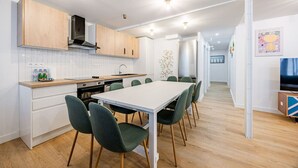 A modern kitchen with wooden cabinets, a white countertop, and a dining area with a white table and green chairs. - Appart 8pers # 3 Bedrooms # Pereire # Paris 17 (Paris)