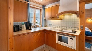 A compact kitchen with wooden cabinets, a sink, a stove, and a window with curtains.
