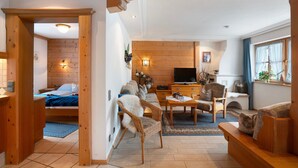 A wooden-paneled room with a bed, a sofa, a TV, and a dining area.