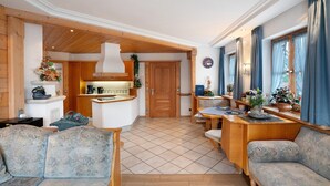 Un'ampia zona giorno con soffitto in legno, una cucina sullo sfondo e un'area pranzo con tavolo e sedie.