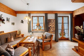 Ein gemütliches Wohnzimmer mit Sofa, Sessel, Couchtisch aus Holz und Kamin.