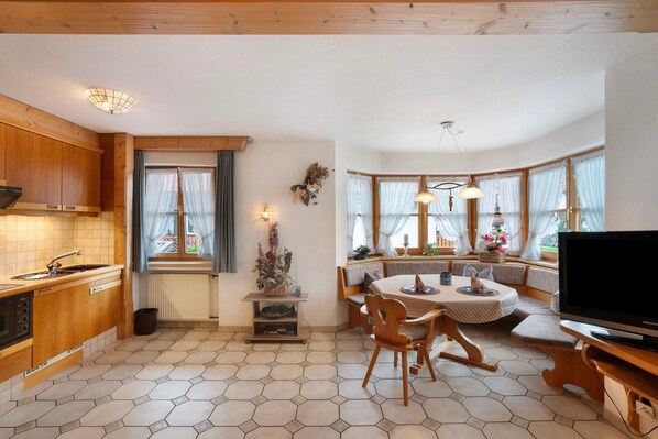 A cozy kitchen with wooden cabinets, a dining area with a round table and chairs, and a large window with curtains.