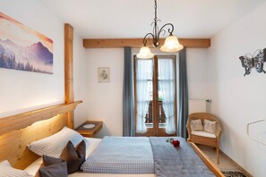 A bedroom with a wooden headboard, a bed with checkered bedding, a wicker chair, and a butterfly wall decoration.