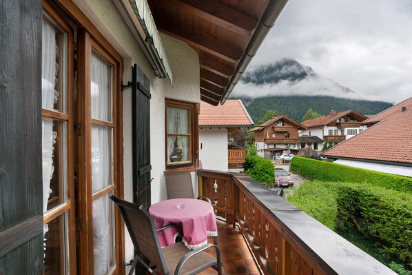 A balcony with a table and chair, a view of a mountain, and traditional chalet-style buildings.