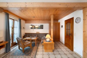 A cozy room with wooden ceiling beams, a sofa, a table with a lamp, and a clock on the wall.