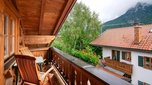 A wooden balcony with chairs, a table, and a view of a mountain and greenery. - Apartment 'Edelweiß Nr 5' with Mountain View, Shared Garden and Wi-Fi (Mittenwald)