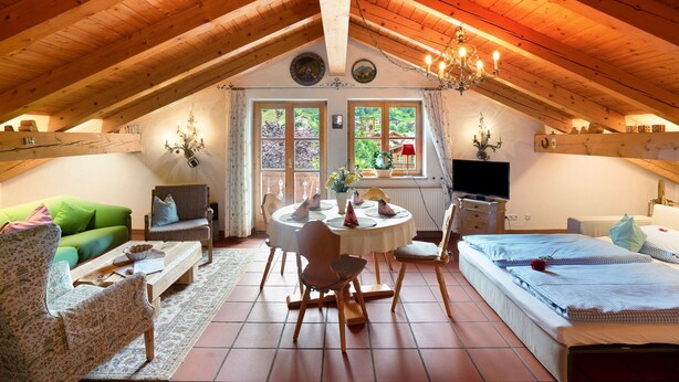 A cozy attic room with a wooden ceiling, a round dining table, a bed, and a television. - Apartment 'Edelweiß Nr 5' with Mountain View, Shared Garden and Wi-Fi (Mittenwald)